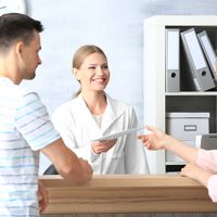 Young female receptionist with clients in hospital