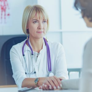 Smiling doctor looking at a patient on a wheelchair in hospital hallway.